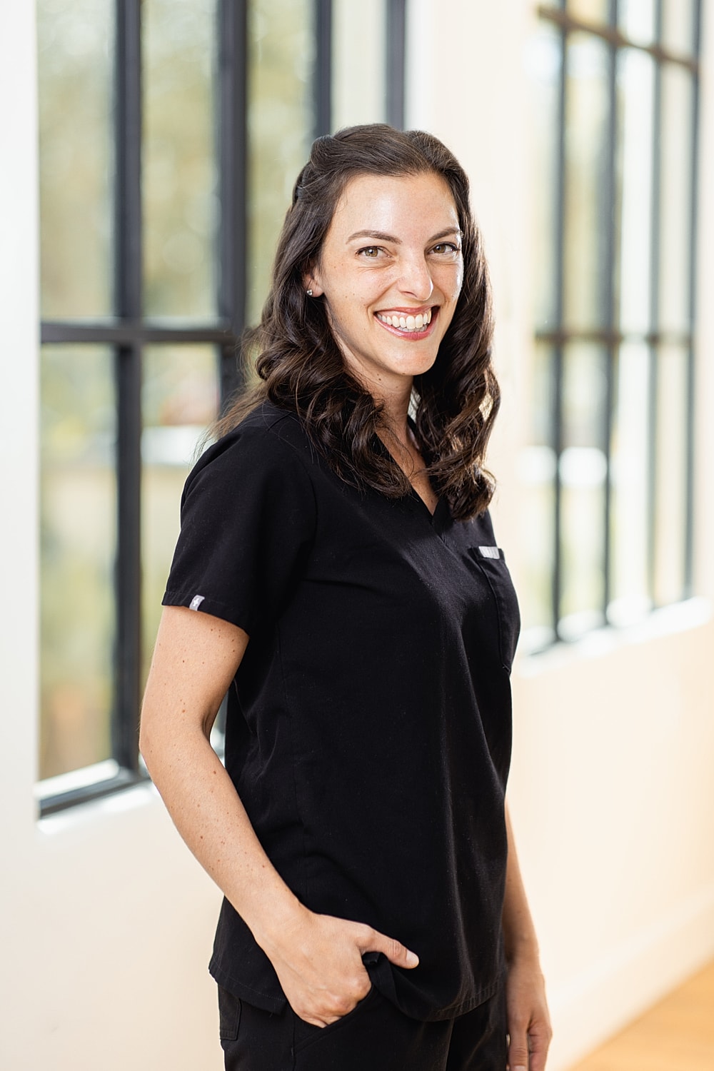 Smiling woman in black scrubs against bright background.