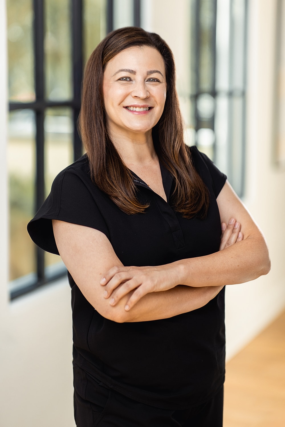 Smiling woman with arms crossed, indoor setting.